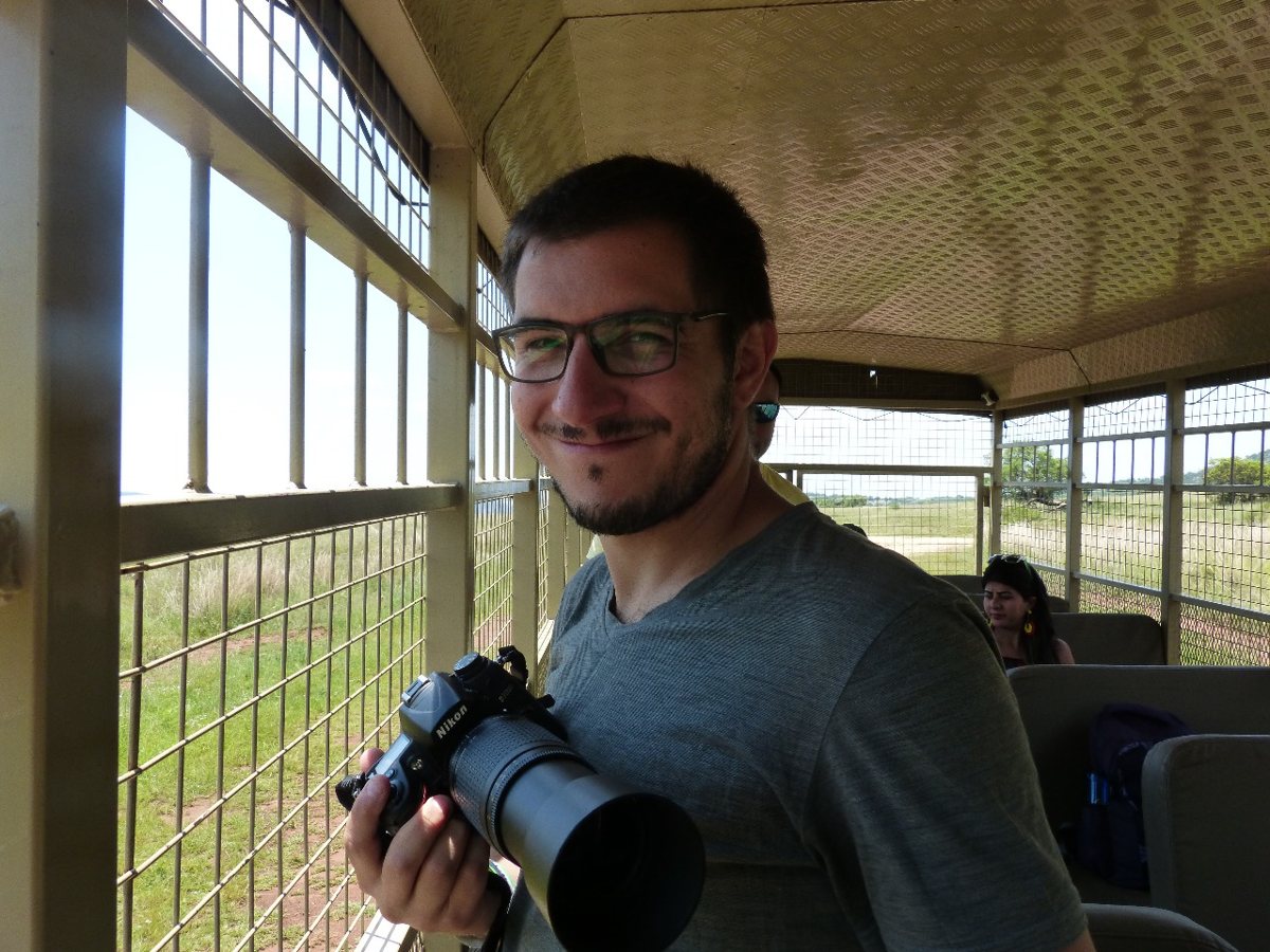 Alex Fisberg, sorrindo, com uma câmera fotográfica nas mãos