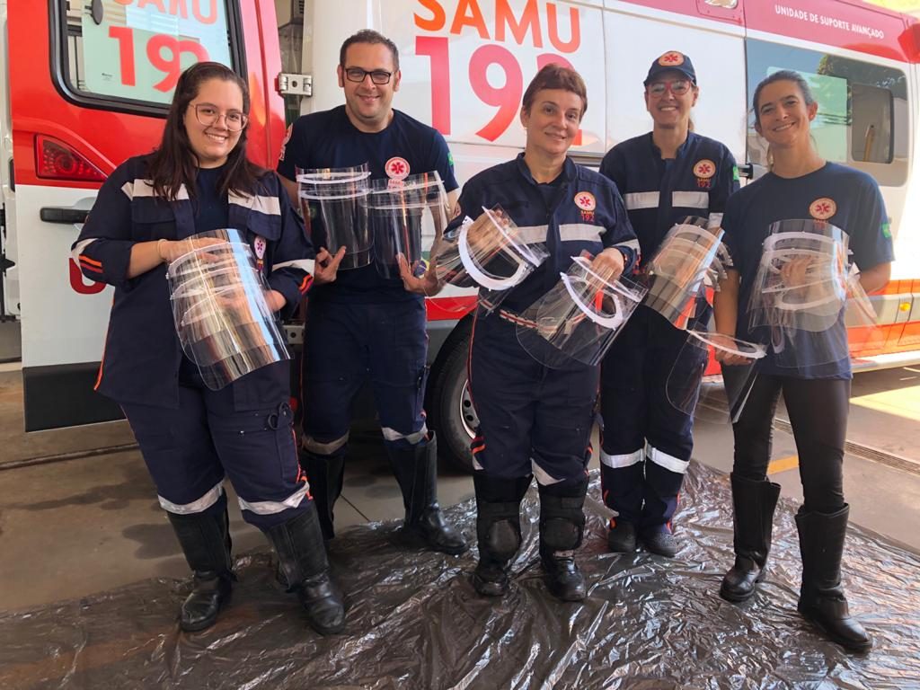 Equipe do SAMU segura face shields doadas pela campanha, em frente a uma ambulância