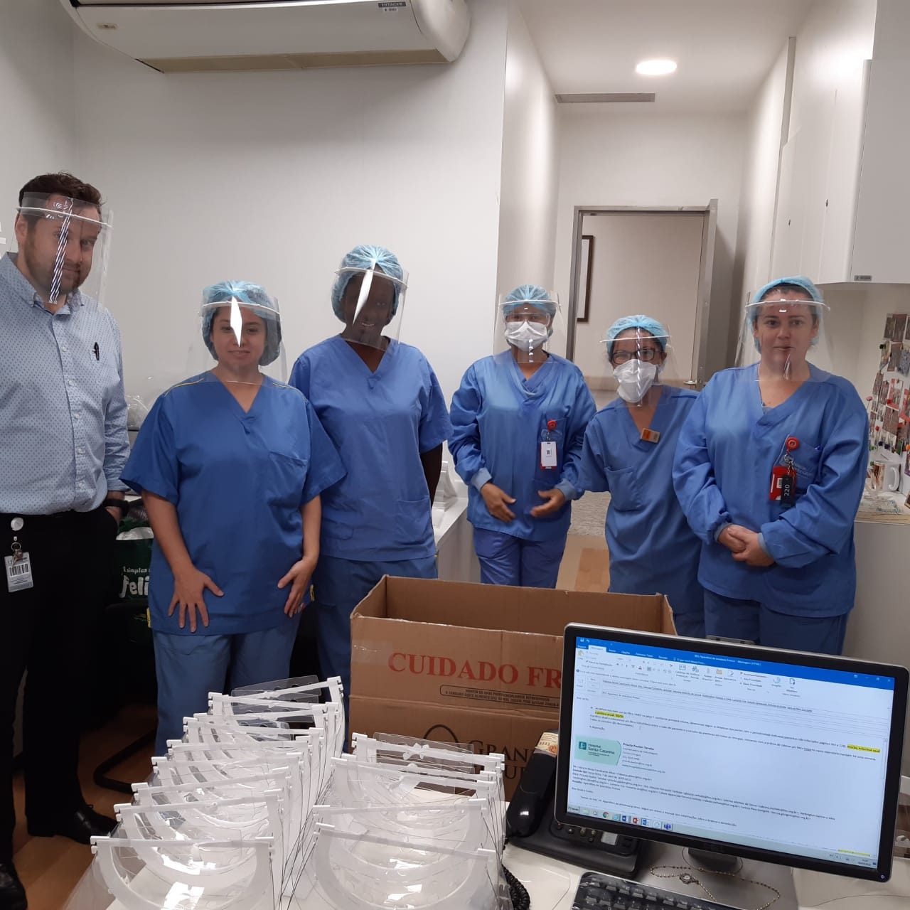 Profissionais de saúde de um hospital usando face shields, ao lado de caixas com mais protetores para distribuir