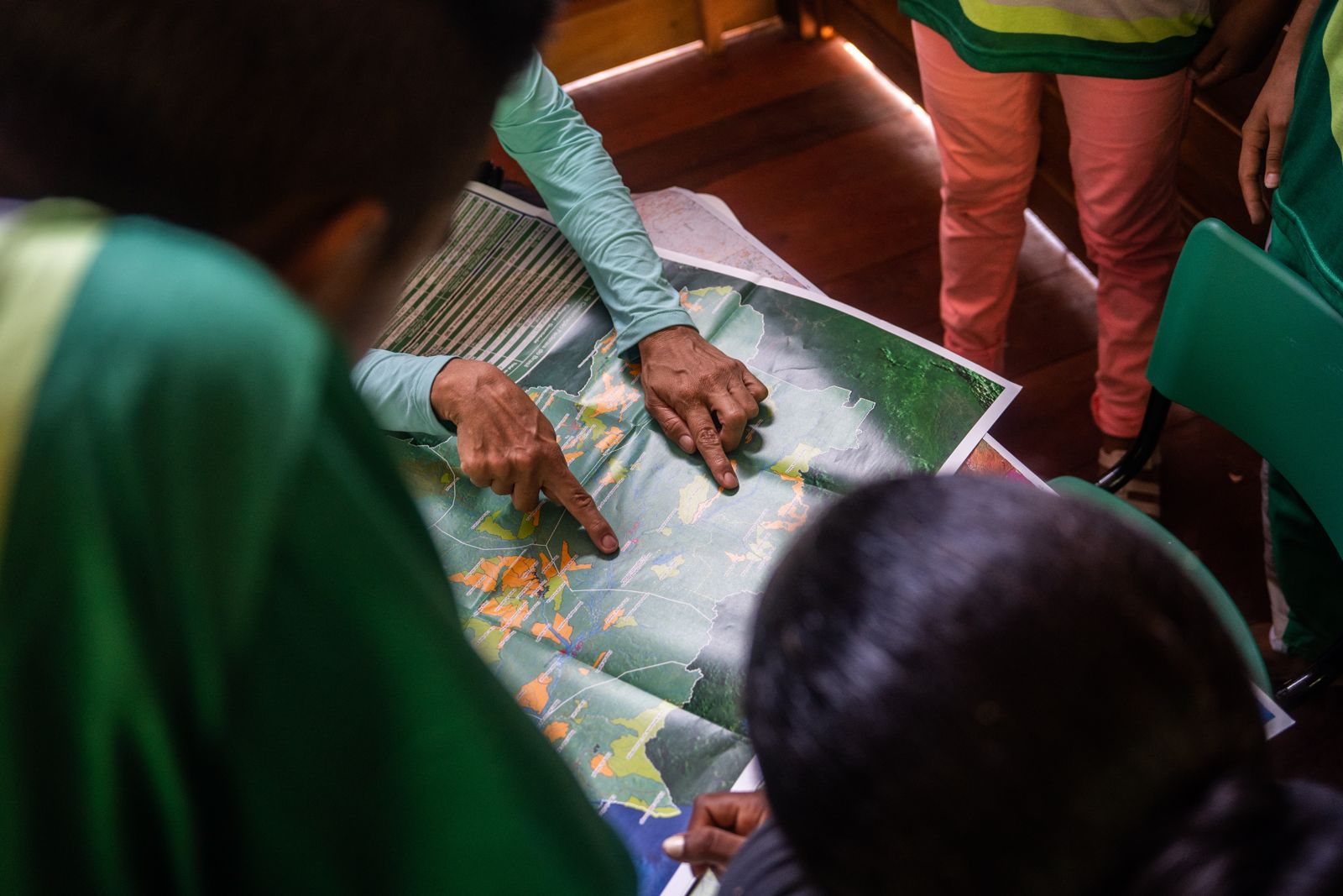 Crianças de uniforme verde numa sala de aula de madeira da Escola Araçari; um menino sorri para a câmera