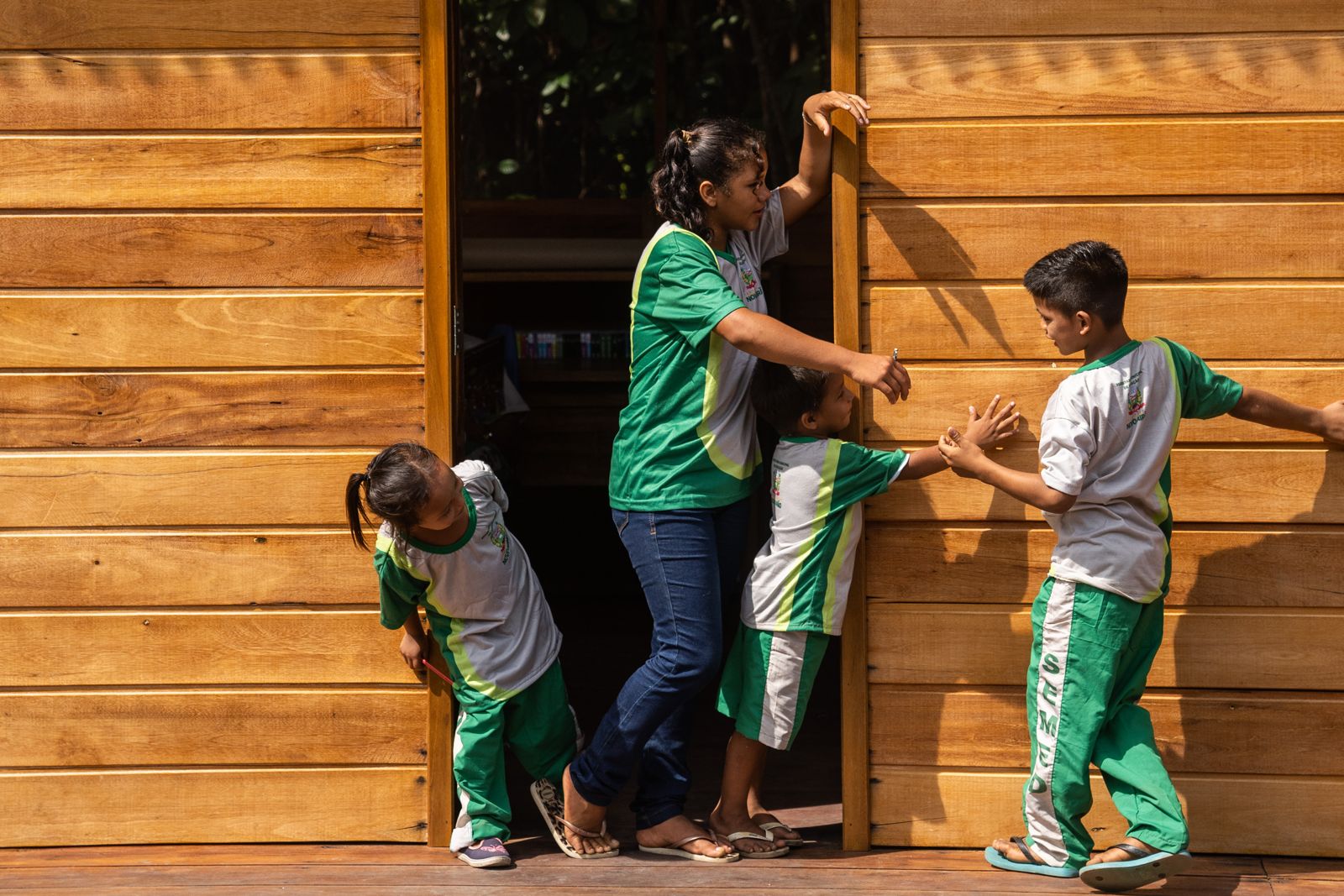 Professora e alunos da Escola Araçari brincam junto à porta de madeira da escola