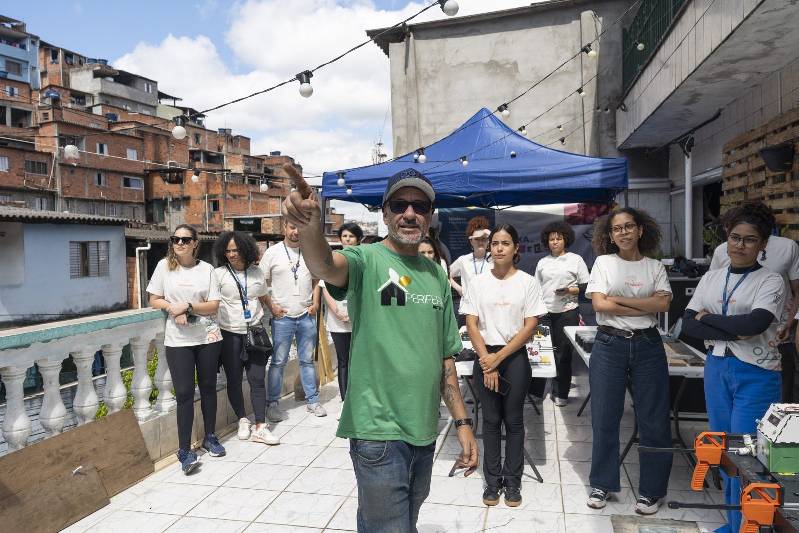 Morador e líder comunitário com camiseta da Periferia Sustentável explica o projeto a voluntários da L'Occitane numa laje na periferia de São Paulo