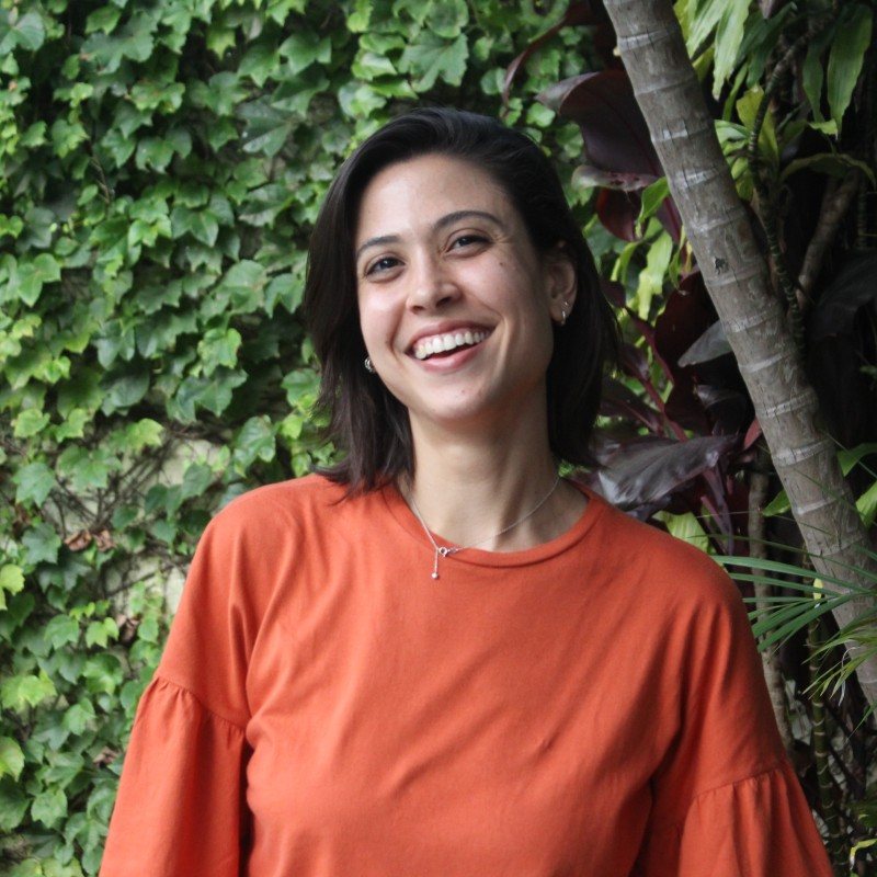 Manuela Beserra, sorrindo, em frente a uma parede de folhagens