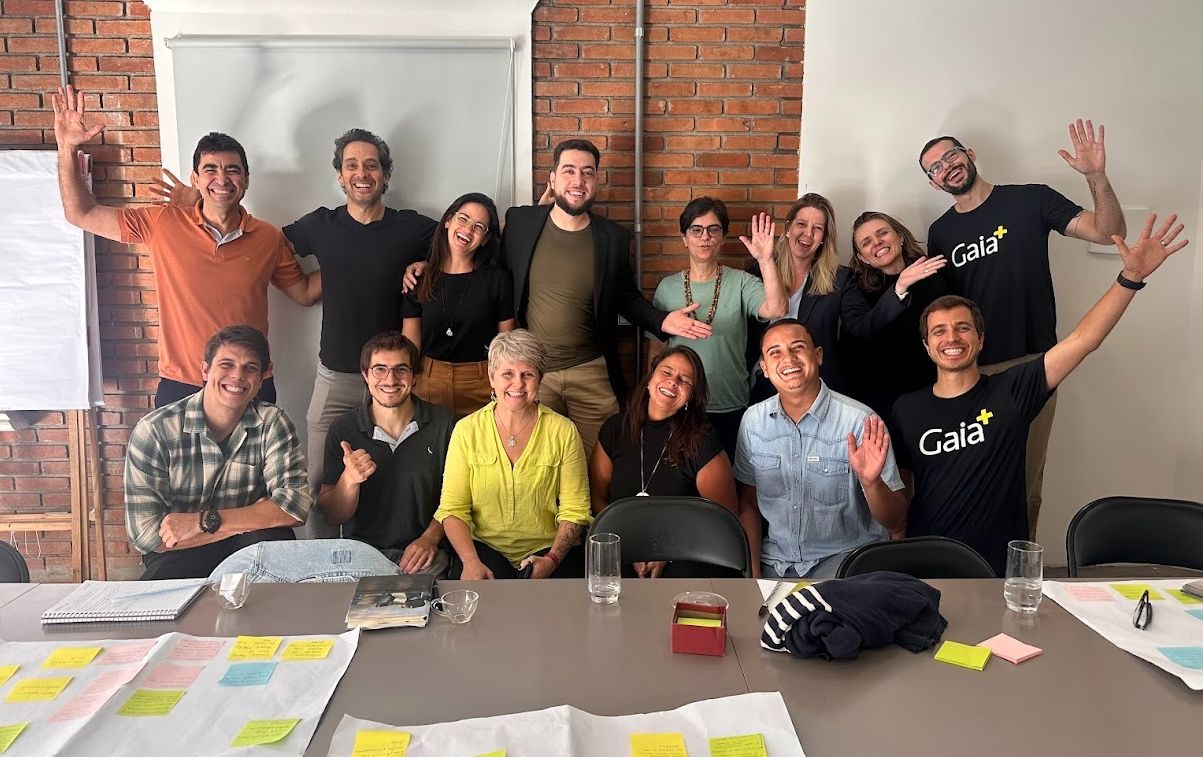 Participantes do workshop do Fundo Pranay posam juntos e sorrindo em volta da mesa de trabalho