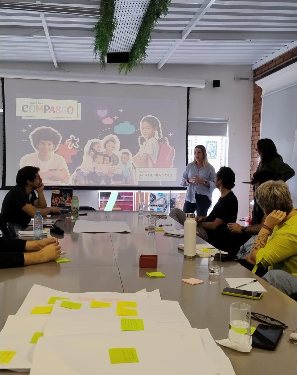 Apresentação de uma das iniciativas apoiadas no telão, com post-its espalhados pela mesa