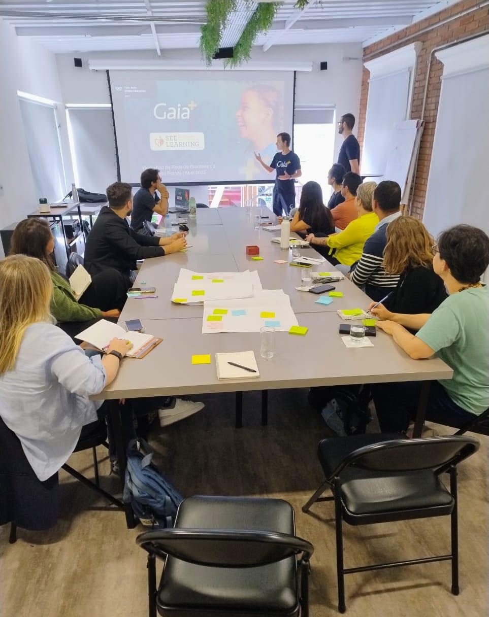 Sala do workshop com participantes em volta da mesa acompanhando uma apresentação